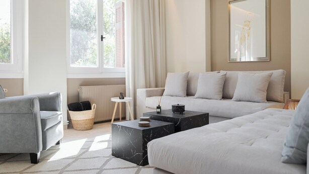 En moderne stue med en grå sofa, en hvid sofa og en grå lænestol. Der er to sorte sofaborde i marmor, en fletkurv og et lille hvidt sofabord.