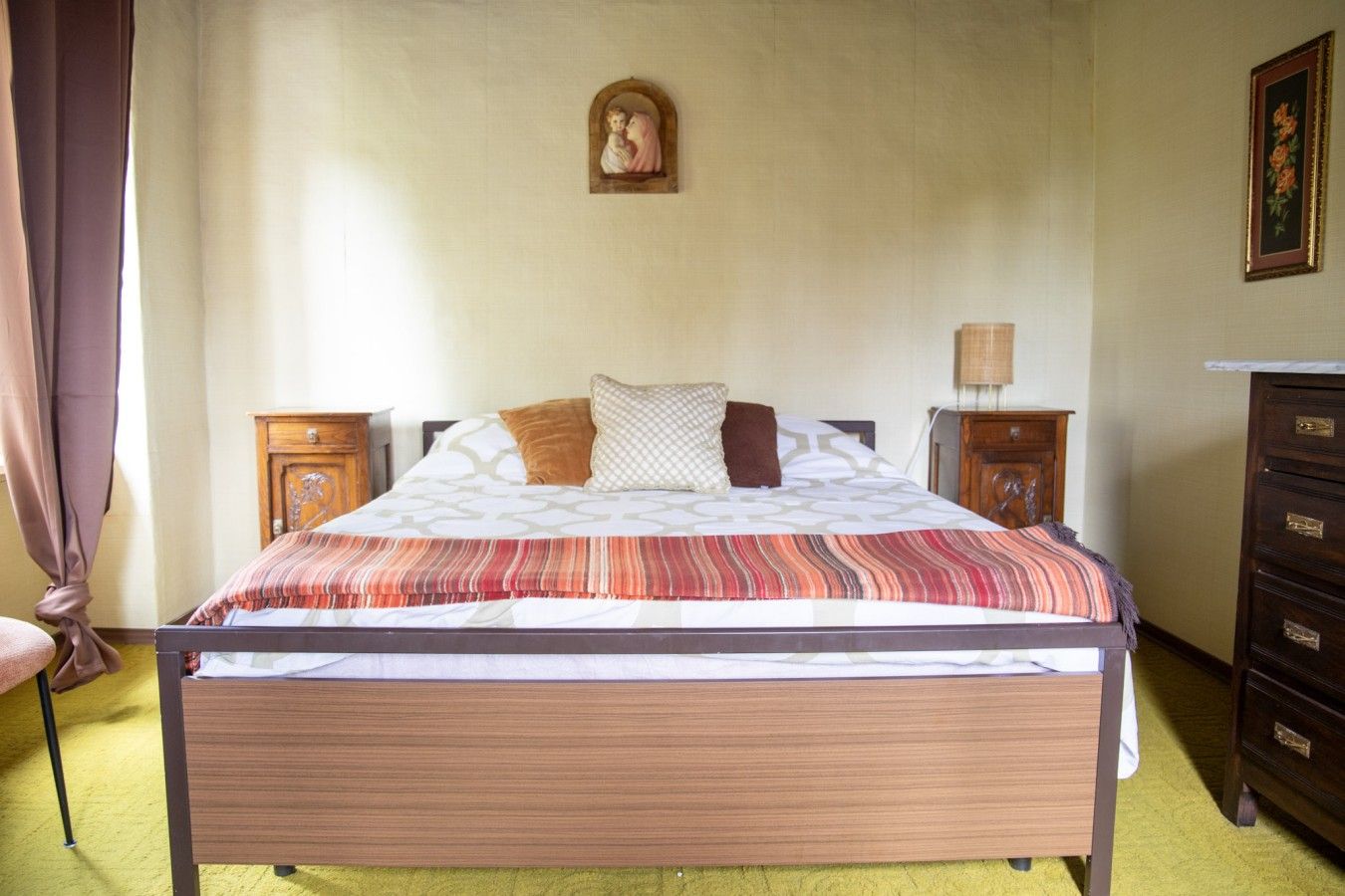 Ein Schlafzimmer mit einem Bett, Nachttischen, einer Kommode, einer Wandlampe und einem gerahmten Bild.