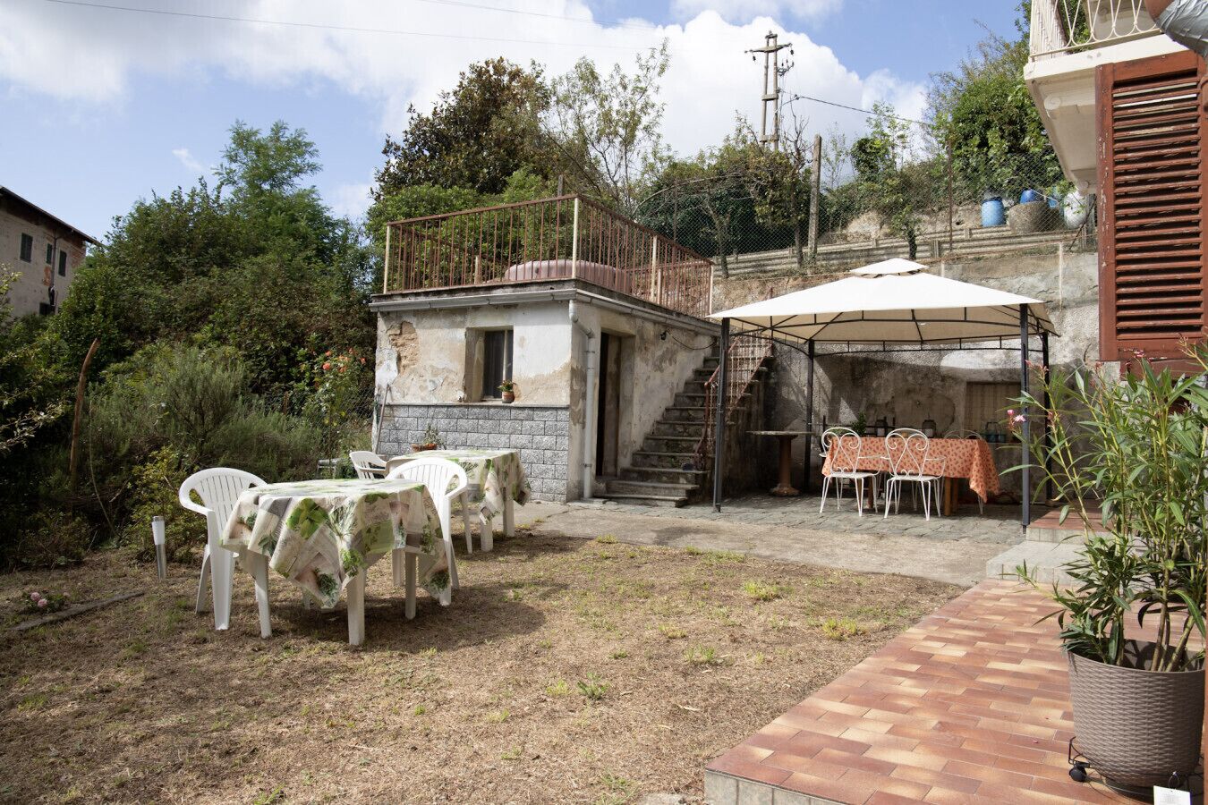 A rustic outdoor patio with stone tables and chairs, a covered seating area, and a staircase leading to a balcony.