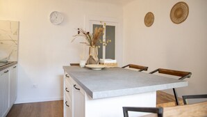 Une cuisine avec un pare-feu en marbre, un îlot central doté de chaises, une horloge et deux éléments décoratifs en fibres tressées accrochés au mur.