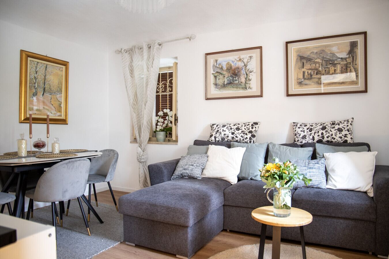 Un salon avec un canapé gris, une table à manger avec des chaises et des œuvres d’art encadrées accrochées aux murs.