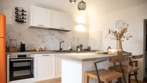 Une cuisine moderne avec des meubles blancs, un four encastré, un dosseret en marbre et un coin bar avec des tabourets.