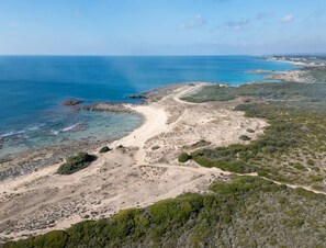Vue aérienne d’un paysage côtier avec un sentier de terre menant à la mer, entouré d’une végétation clairsemée et d’un terrain rocheux.