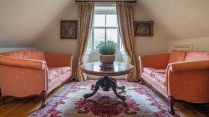 A room with two plush armchairs, a round table with a plant, and a large window with curtains. - Penninghame Estate - Tower Apartment (Penninghame)