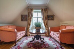 A room with two plush armchairs, a round table with a plant, and a large window with curtains. - Penninghame Estate - Tower Apartment (Penninghame)