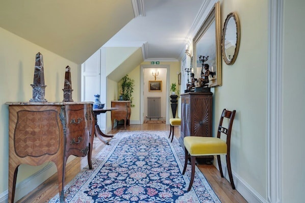 Un pasillo con alfombra estampada, muebles de madera y un espejo en la pared.