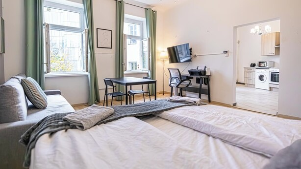 A hotel room with a bed, a desk, a chair, a TV, and a kitchenette. - Spacious 1BR Apt Near Danube (Vienna)