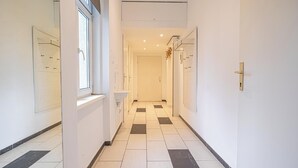 A narrow hallway with white walls, a checkered floor, and a window on the left. - Spacious 1BR Apt Near Danube (Vienna)