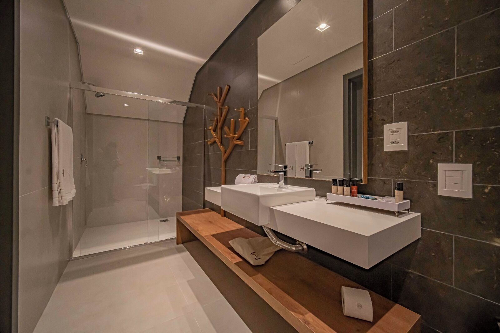 Un baño moderno con cabina de ducha de vidrio, dos lavamanos y un espejo grande.