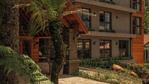 A multi-story building with a wooden facade, large windows, and a landscaped garden with ferns. - Harmont Hotel (Gramado)