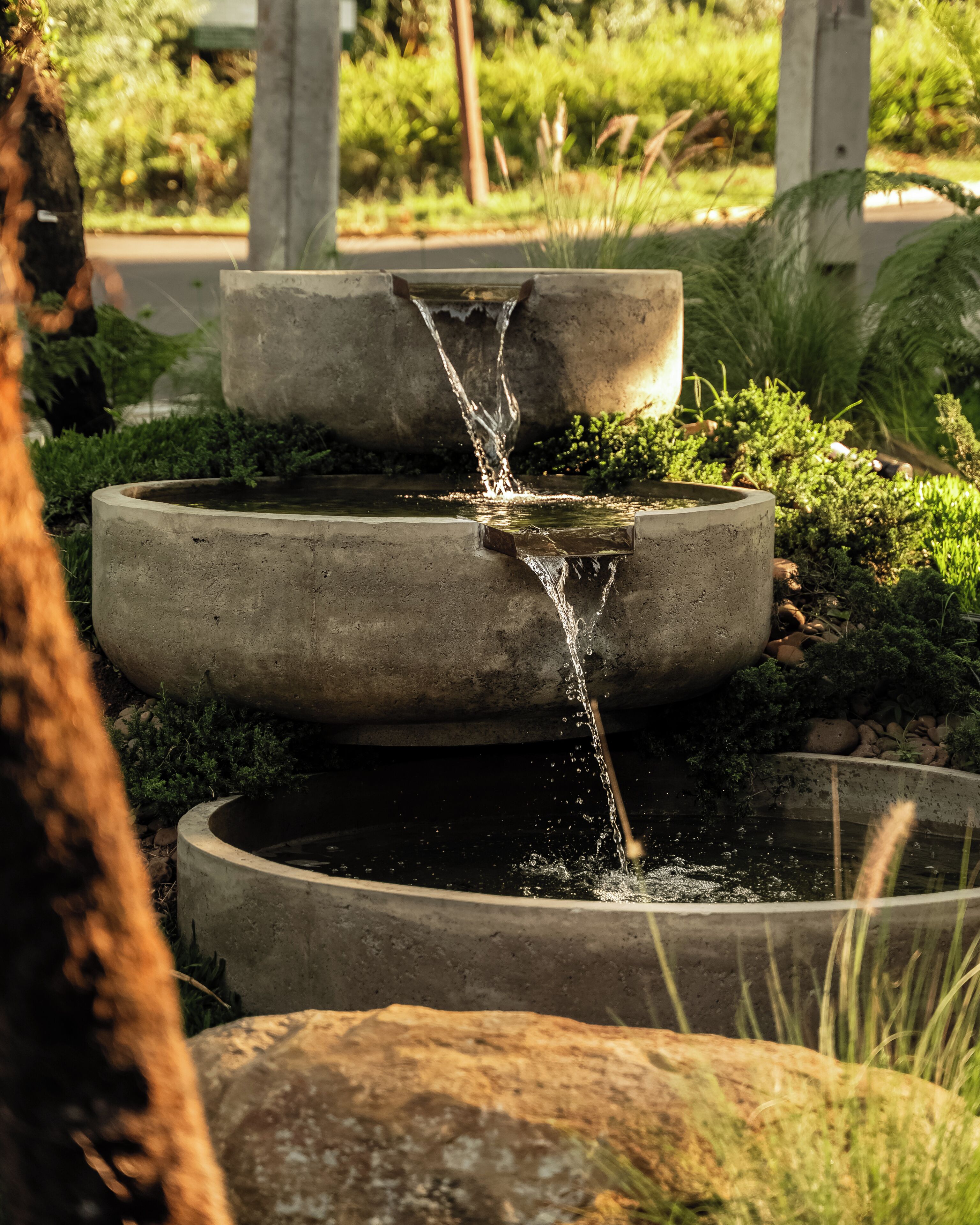 Una fuente de hormigón escalonada con agua en cascada, rodeada de follaje.