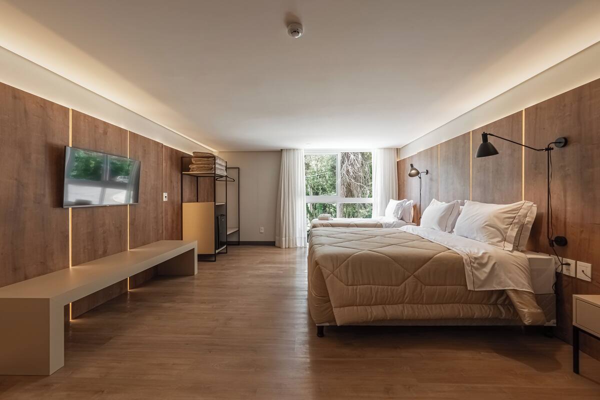 A modern bedroom with a large bed, a TV mounted on the wall, a bench, and a bedside table.