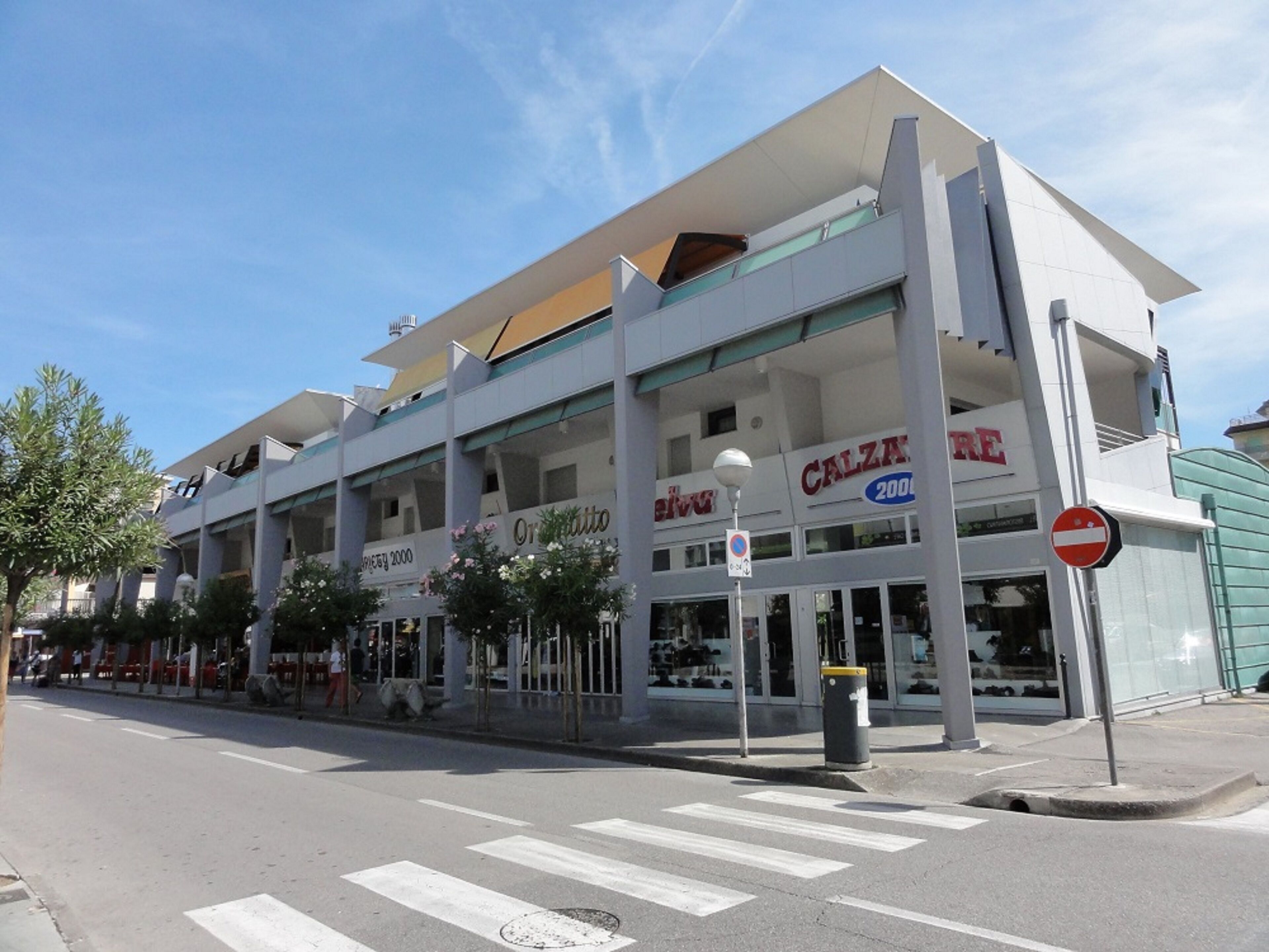 Un edificio de varios pisos con un diseño arquitectónico moderno, que presenta un letrero llamativo de 'Calzature' en la planta baja.