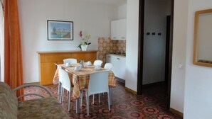 A compact living space with a dining area, kitchenette, and a door leading to another room. - Apartment in a villa with balcony (Bibione)