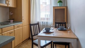 A small kitchen with wooden cabinets, a dining table with chairs, and a window with sheer curtains. - AS HOME Nożownicza (Wrocław)