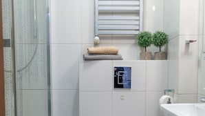 A modern bathroom with a glass shower enclosure, a toilet, a sink, and a small window with blinds. - AS HOME Nożownicza (Wrocław)