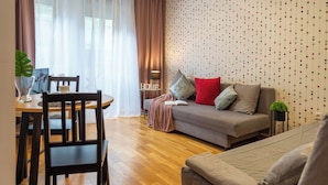 A modern living room with a sofa, a dining table with chairs, and a decorative plant. - AS HOME Nożownicza (Wrocław)