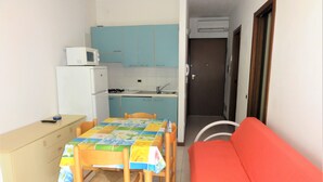 A compact kitchen with a microwave, stove, and sink, a dining table with chairs, and a red sofa.