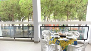 A balcony with a table set for dining, surrounded by white chairs, and overlooking a street with trees.