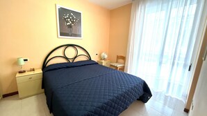Een slaapkamer met een bed, nachtkastje, stoel, lamp en raam met gordijnen.
