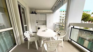 Een balkon met een ronde tafel en witte plastic stoelen, een wasmachine en een kleine keukenhoek.