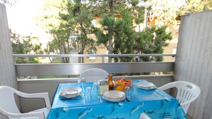 Ein Balkon mit einem Tisch, der mit Tellern, Gläsern und einem Obstkorb gedeckt ist, umgeben von weißen Stühlen.