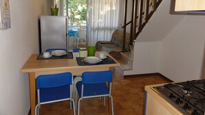Kompakti keittiö, jossa on ruokapöytä, tuolit, jääkaappi ja liesi.