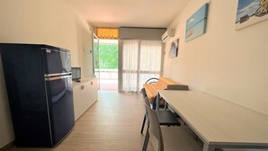 Eine kleine Küche mit Kühlschrank, einem Esstisch und Stühlen. Eine Glastür führt in einen Außenbereich.