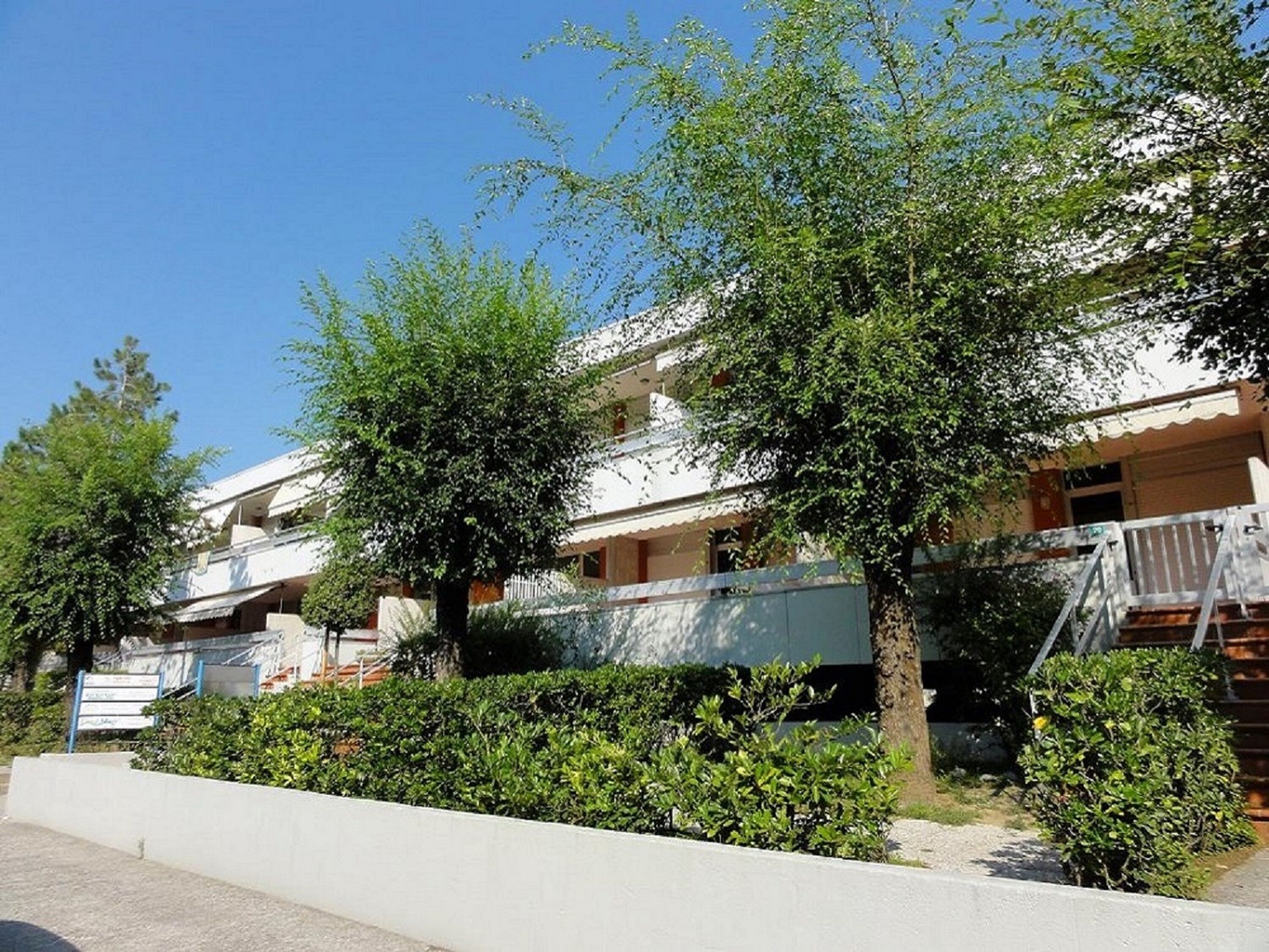 Un edificio residencial con varios balcones, fachada blanca y abundante vegetación.