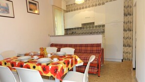 A dining area with a table set for four, white chairs, a red and yellow floral tablecloth, and a red plaid sofa. - Apartment in villa with fenced garden (Bibione)