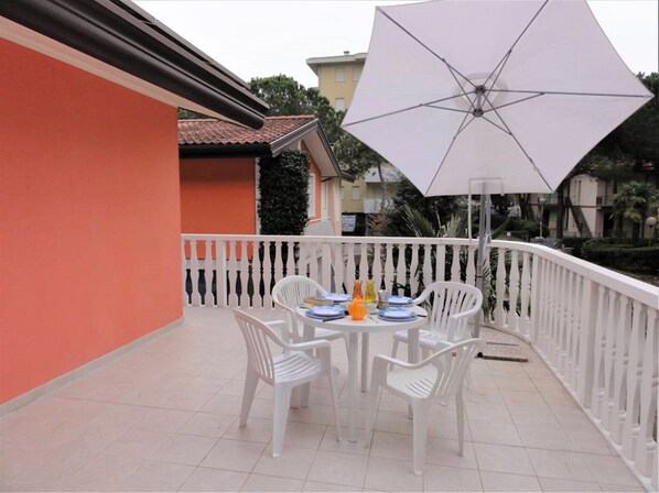 A balcony with a table and chairs, a large umbrella, and a white railing.