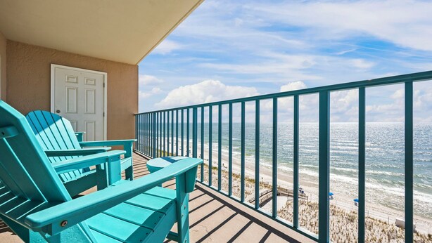 Ein Balkon mit türkisfarbenen Adirondack-Stühlen, einer weißen Tür und Blick auf Strand und Meer.