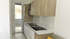 A compact kitchen with wooden cabinets, a stainless steel sink, and a white countertop. - Bright flat with pool and balcony (Bibione)