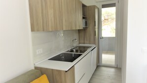 A compact kitchen with wooden cabinets, a stainless steel sink, and a grey countertop. - Bright flat in a villa with shared pool (Bibione)