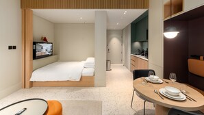 A modern hotel room with a bed, a TV, a dining area with a table set for two, and a kitchenette. - Urban Studio w Balcony Near Downtown and Canal (Dubai)