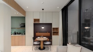 A modern living room with a round dining table, two chairs, a sofa, and a large window. - Urban Studio w Balcony Near Downtown and Canal (Dubai)