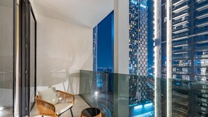 A balcony with wicker chairs and a glass partition, overlooking a cityscape at night. - Urban Studio w Balcony Near Downtown and Canal (Dubai)