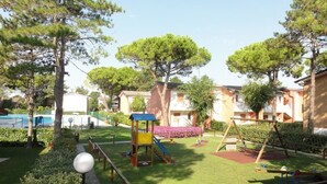 A playground with a slide, swing set, and climbing structure surrounded by well-maintained grass and trees.
