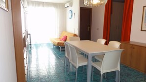 Ein Essbereich mit weißem Tisch und Stühlen, einem blauen Fliesenboden, einem Bett mit gelber Tagesdecke und einem roten Vorhang.