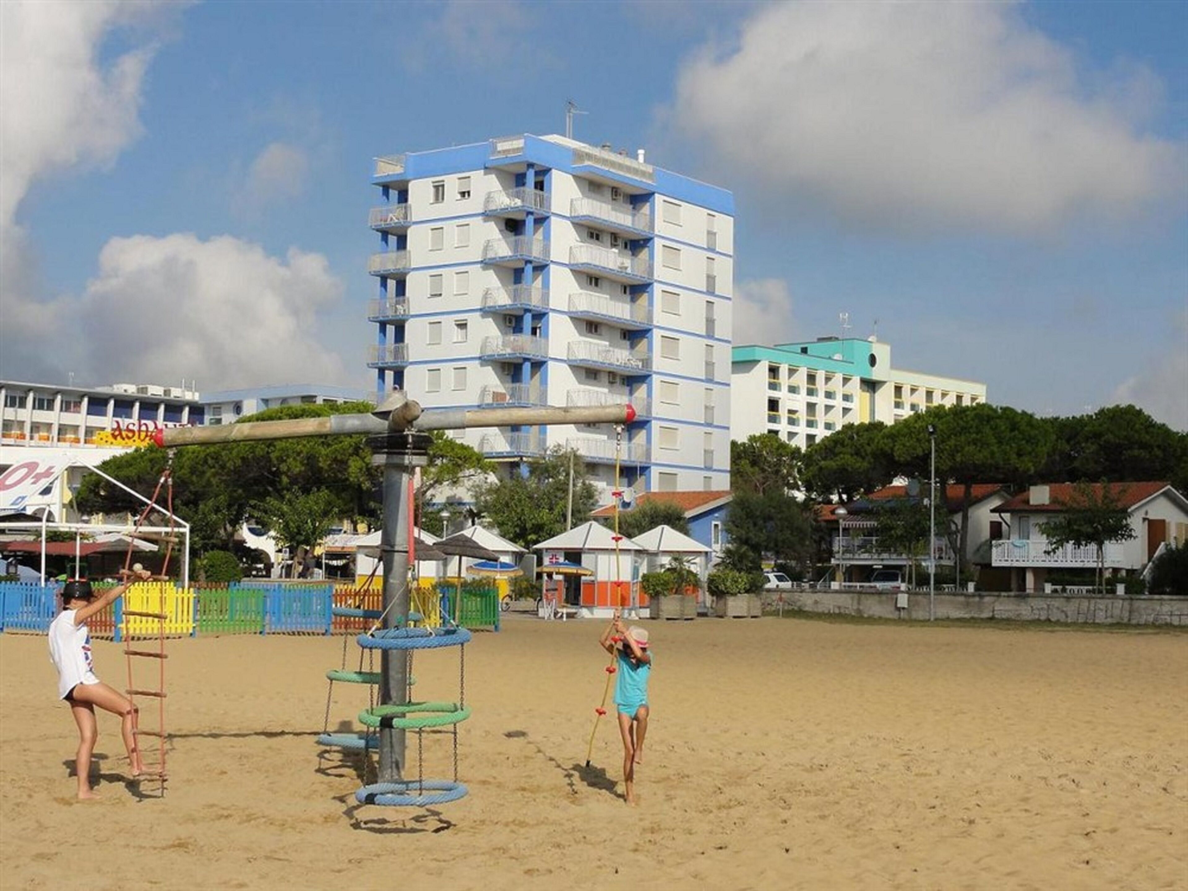 A beach with a playground, a tall building, and a few houses in the background.
