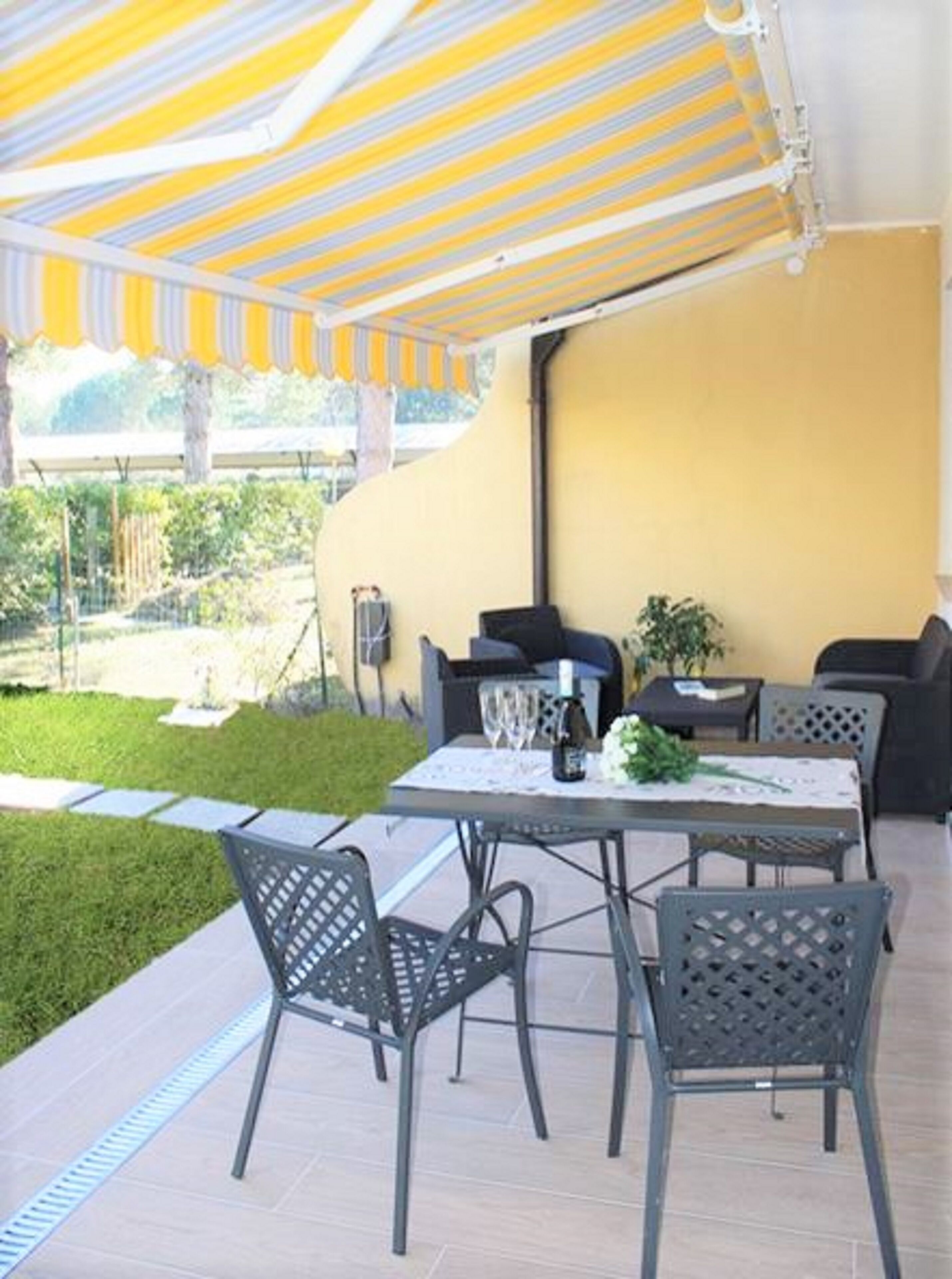 Une terrasse extérieure avec une table et des chaises, un mur jaune et un auvent à rayures.