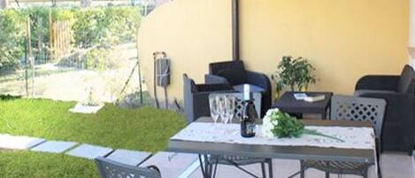 Une terrasse extérieure avec une table et des chaises, un mur jaune et un auvent à rayures.