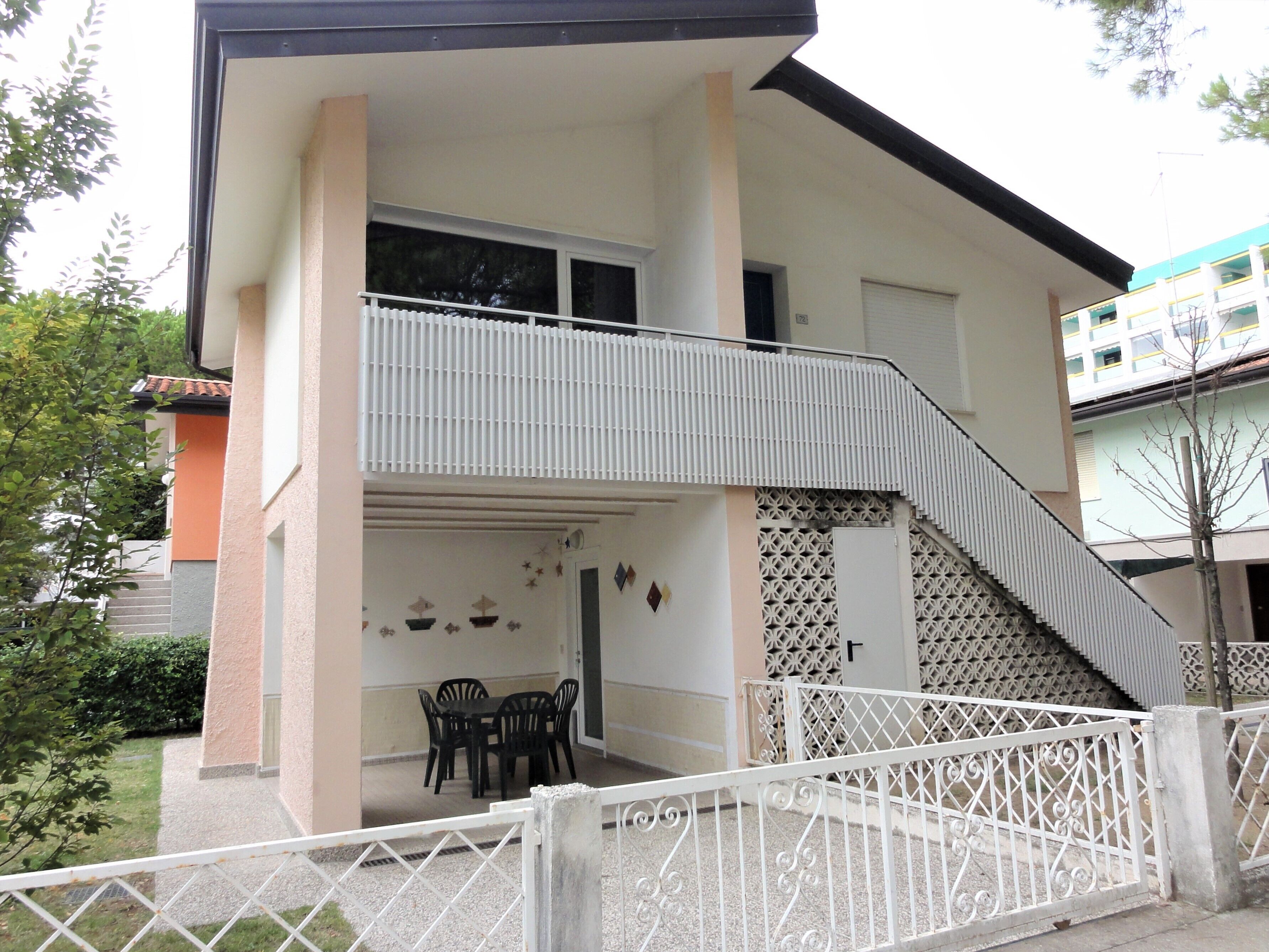 A two-story building with a balcony, a staircase, and a patio area with chairs.