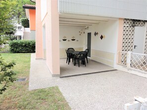 A covered patio area with a table and chairs, a small garden, and a white gate.