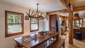 A spacious kitchen with a wooden table, a chandelier, and large windows. - The Moose’s Retreat - nestled in the trees in the Aspens. (Wilson)