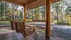 A wooden swing hanging from a porch with a view of a forested area. - The Moose’s Retreat - nestled in the trees in the Aspens. (Wilson)