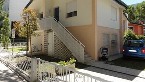 Um edifício de dois andares com fachada branca e bege, uma escadaria e uma pequena área ajardinada.