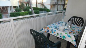 Uma varanda com mesa e cadeiras, um cercado branco e um edifício ao fundo.