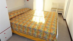 Une petite pièce, bien éclairée, avec un lit, une chaise et un miroir au mur.