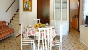 A dining area with a table set for two, a sofa, and a staircase leading to another room.